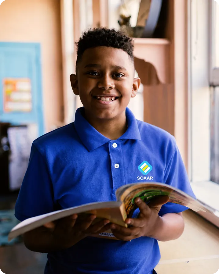 SOAAR student smiling while holding an open book